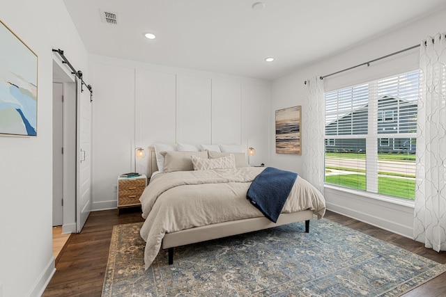 bedroom with a barn door and dark hardwood / wood-style floors