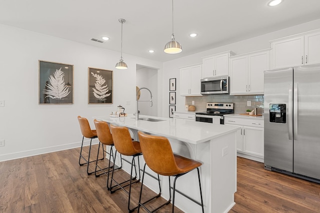 kitchen featuring pendant lighting, a center island with sink, sink, dark hardwood / wood-style floors, and appliances with stainless steel finishes