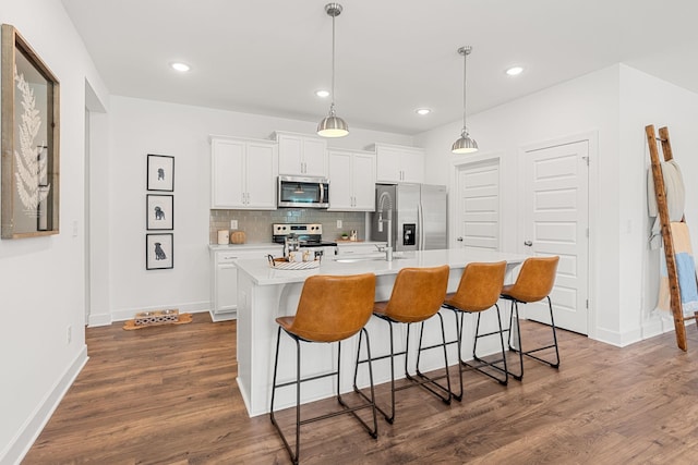 kitchen featuring white cabinets, dark hardwood / wood-style floors, stainless steel appliances, and an island with sink