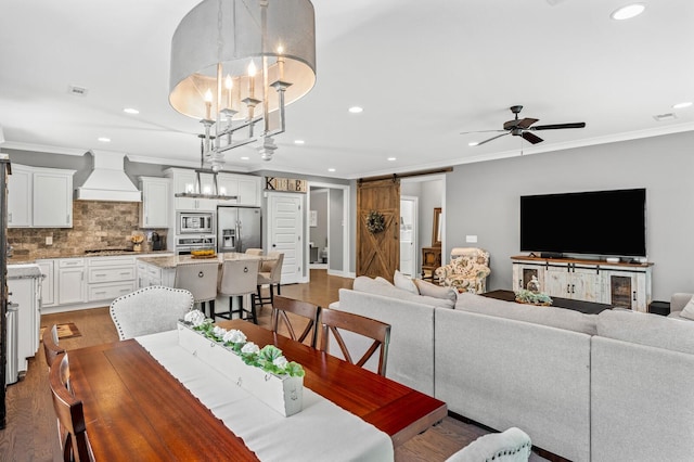 dining area featuring a barn door, ornamental molding, ceiling fan with notable chandelier, and hardwood / wood-style flooring