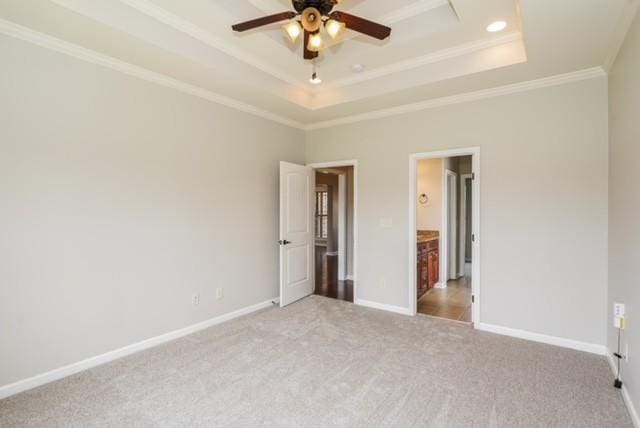 unfurnished bedroom featuring a raised ceiling, crown molding, connected bathroom, and light colored carpet