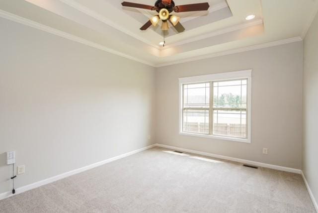 empty room featuring a tray ceiling, carpet floors, ornamental molding, and ceiling fan