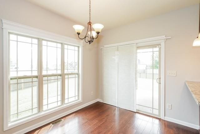 unfurnished dining area featuring a notable chandelier, dark wood-type flooring, and a healthy amount of sunlight