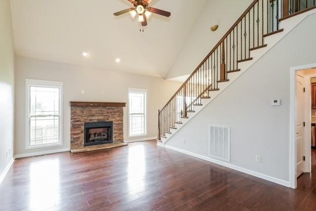 unfurnished living room with dark wood-type flooring, ceiling fan, a stone fireplace, and high vaulted ceiling