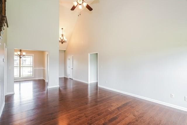 unfurnished living room with ceiling fan with notable chandelier, dark wood-type flooring, and a high ceiling