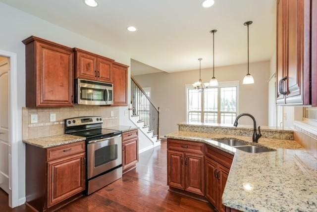 kitchen with sink, backsplash, hanging light fixtures, stainless steel appliances, and light stone counters