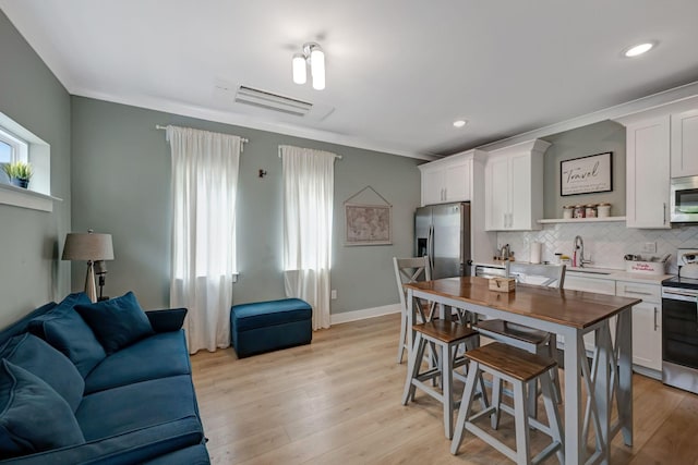 kitchen with white cabinets, light wood-style flooring, appliances with stainless steel finishes, light countertops, and backsplash