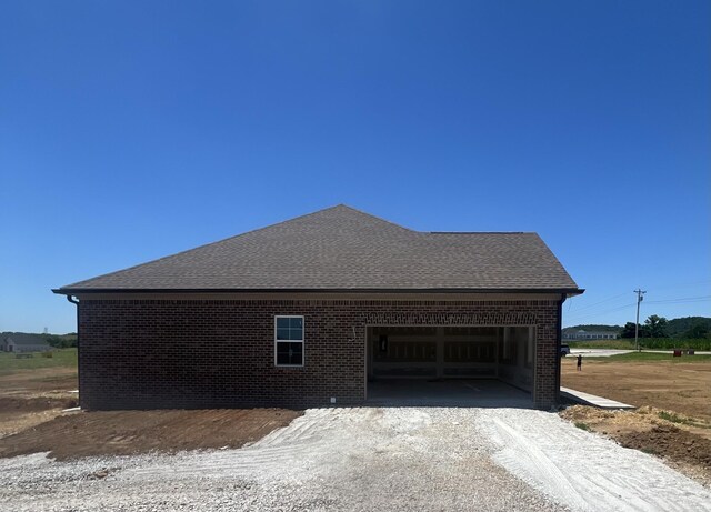 view of property exterior featuring a garage, roof with shingles, and brick siding