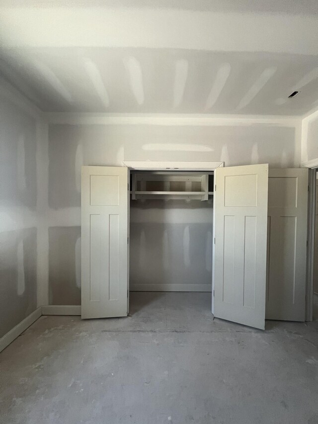 unfurnished bedroom featuring concrete flooring, a closet, and baseboards