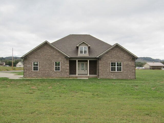 view of front of house with brick siding, a front yard, and a shingled roof