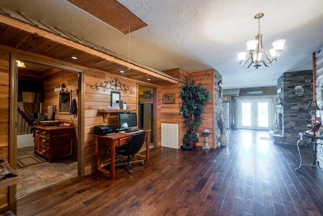 interior space featuring french doors, a textured ceiling, dark wood-type flooring, a chandelier, and wood walls