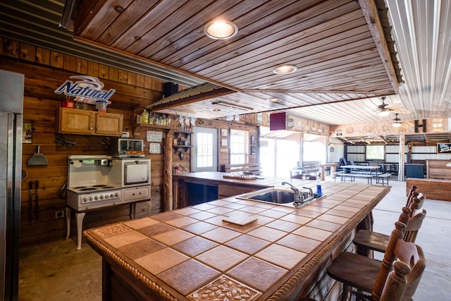 kitchen with tile countertops, wood walls, sink, and a wealth of natural light