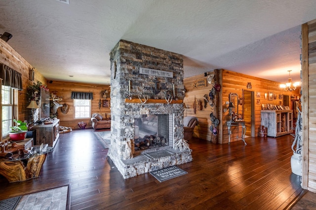 living room featuring wood walls, a stone fireplace, log walls, dark hardwood / wood-style flooring, and a chandelier