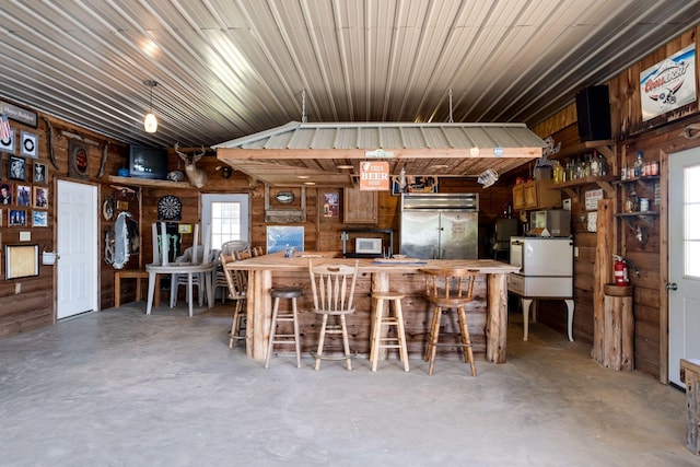 kitchen featuring wood walls, stainless steel built in fridge, lofted ceiling, and concrete floors