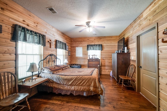 bedroom with ceiling fan, dark hardwood / wood-style flooring, a textured ceiling, and wooden walls