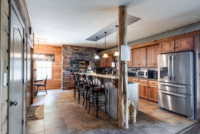 kitchen with light stone countertops, stainless steel refrigerator with ice dispenser, wood walls, pendant lighting, and a breakfast bar