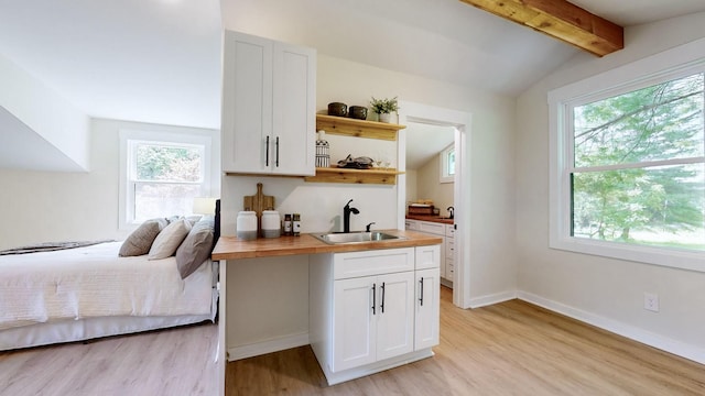 interior space featuring white cabinets, vaulted ceiling with beams, butcher block countertops, and sink