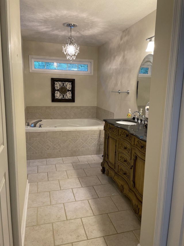 bathroom with an inviting chandelier, vanity, a relaxing tiled tub, and a textured ceiling