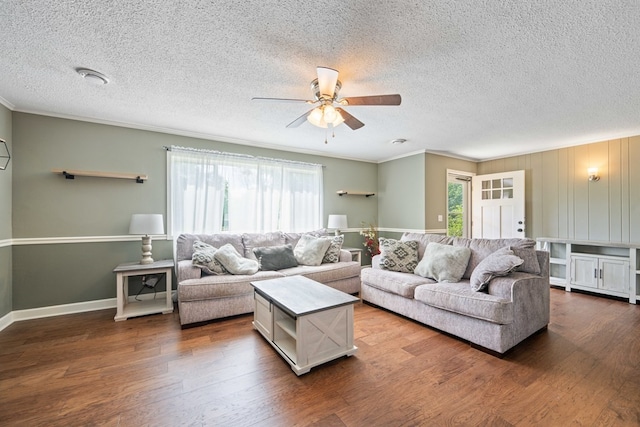 living room with a textured ceiling, dark wood-type flooring, ornamental molding, and ceiling fan