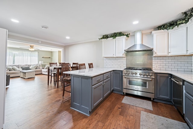 kitchen with wall chimney range hood, dark hardwood / wood-style flooring, stainless steel appliances, white cabinets, and ceiling fan