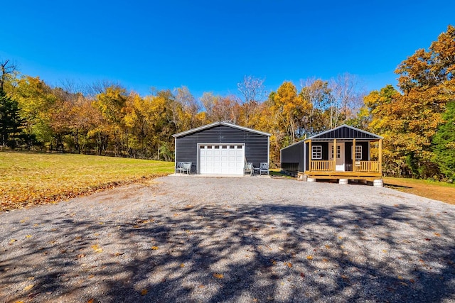 view of front of property featuring covered porch, a garage, an outbuilding, and a front lawn