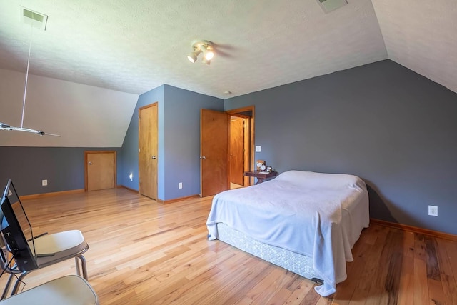 bedroom with a textured ceiling, light hardwood / wood-style flooring, and vaulted ceiling