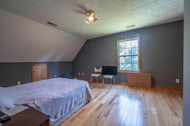 bedroom with a textured ceiling, ceiling fan, light hardwood / wood-style flooring, and vaulted ceiling