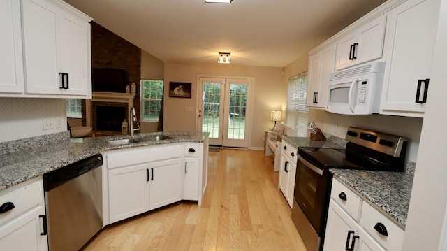 kitchen featuring sink, light stone countertops, appliances with stainless steel finishes, light hardwood / wood-style floors, and white cabinetry