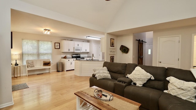 living room featuring a barn door, light wood-type flooring, sink, and high vaulted ceiling