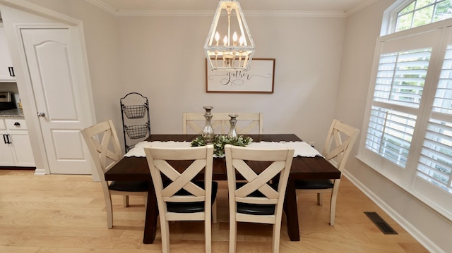 dining space featuring light wood-type flooring, ornamental molding, and a chandelier