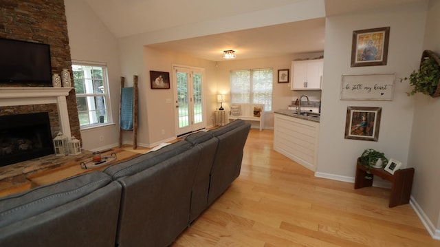 living room with a healthy amount of sunlight, a stone fireplace, light wood-type flooring, and sink