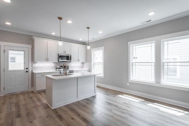 kitchen featuring appliances with stainless steel finishes, white cabinets, sink, pendant lighting, and an island with sink