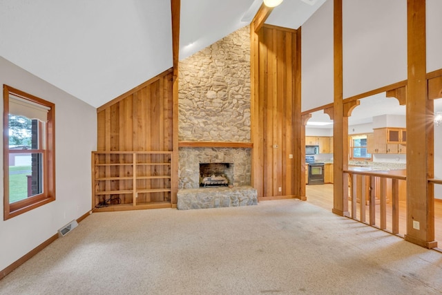 unfurnished living room featuring high vaulted ceiling, a fireplace, wooden walls, and light carpet