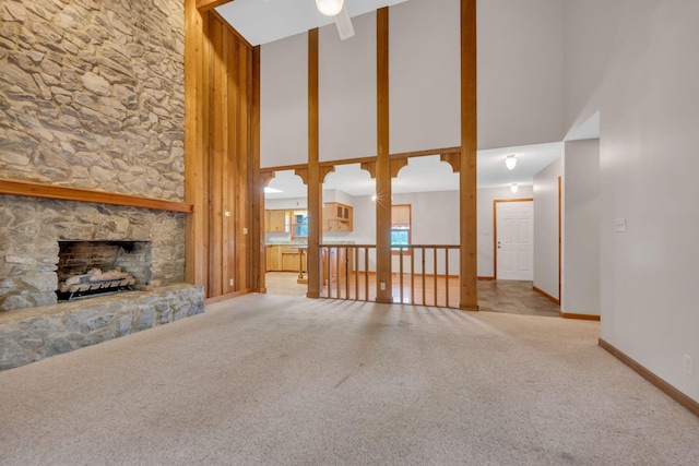 unfurnished living room featuring ceiling fan, a fireplace, light colored carpet, and a high ceiling