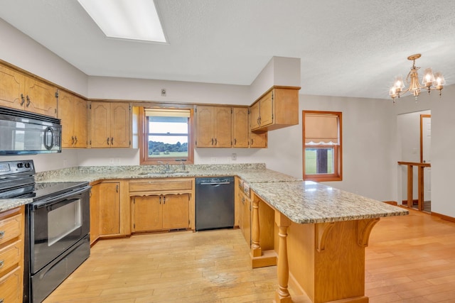 kitchen with black appliances, pendant lighting, an inviting chandelier, light hardwood / wood-style floors, and a breakfast bar area