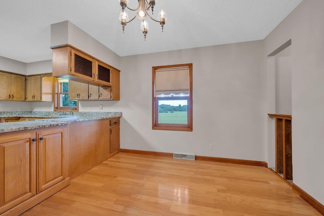 kitchen with a chandelier, a textured ceiling, light wood-type flooring, and light stone countertops