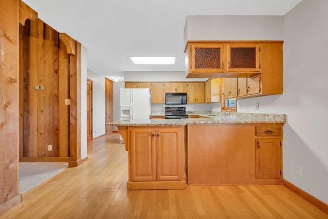 kitchen featuring kitchen peninsula, a skylight, sink, black appliances, and light hardwood / wood-style floors