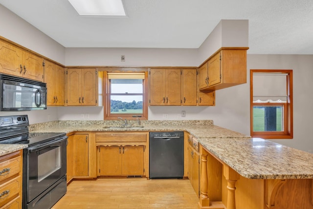 kitchen featuring kitchen peninsula, light stone countertops, light wood-type flooring, sink, and black appliances