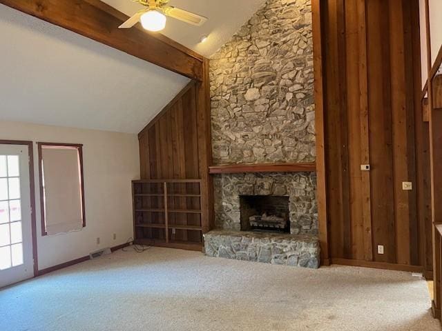 unfurnished living room featuring ceiling fan, a stone fireplace, lofted ceiling with beams, wooden walls, and carpet