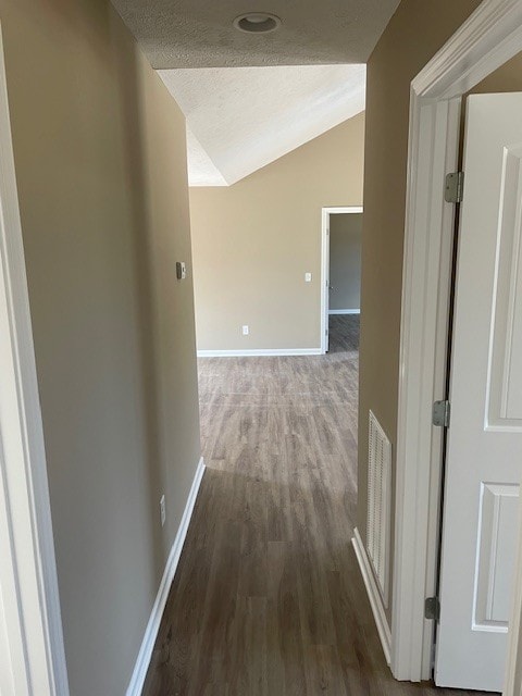 corridor featuring vaulted ceiling, a textured ceiling, and wood-type flooring