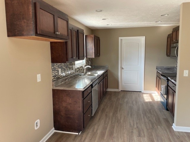 kitchen with stainless steel appliances, sink, decorative backsplash, hardwood / wood-style flooring, and dark brown cabinetry