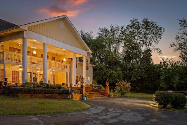 property exterior at dusk featuring ceiling fan, a yard, and a balcony