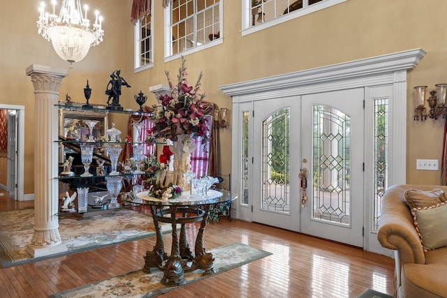 foyer entrance with ornate columns, a towering ceiling, french doors, a notable chandelier, and light hardwood / wood-style flooring