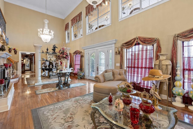 living room featuring a notable chandelier, wood-type flooring, ornamental molding, french doors, and ornate columns