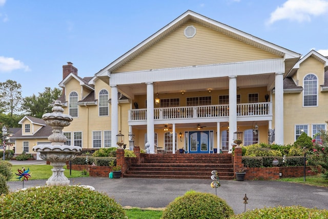 view of front of property with french doors, covered porch, a chimney, and a balcony