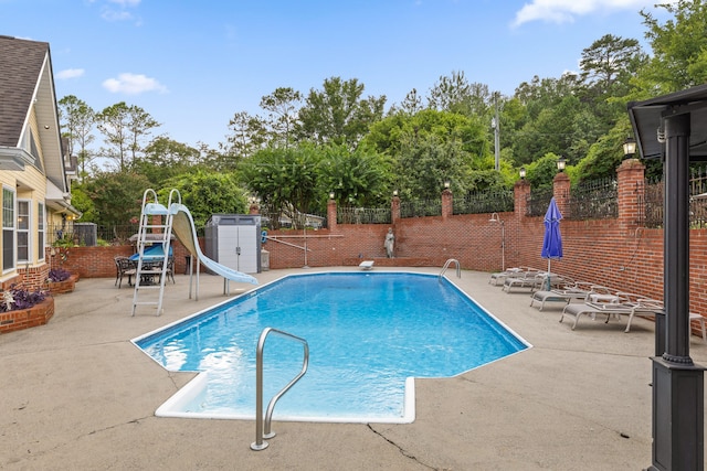 view of swimming pool with a water slide, a diving board, a patio area, and a storage unit