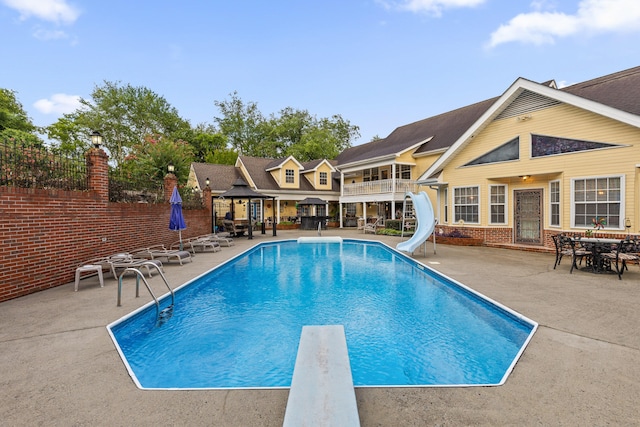 view of pool featuring a water slide, a diving board, and a patio area