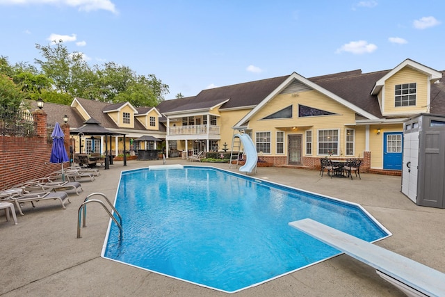 view of pool with a diving board, a gazebo, a water slide, a fenced in pool, and a patio area