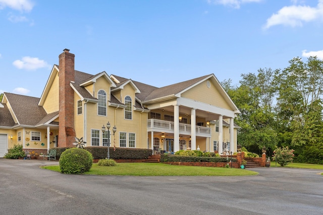 view of front of house with a ceiling fan, a chimney, a balcony, and a front yard