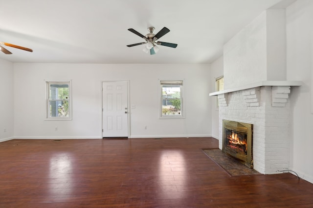 unfurnished living room with brick wall, a brick fireplace, dark hardwood / wood-style flooring, and ceiling fan